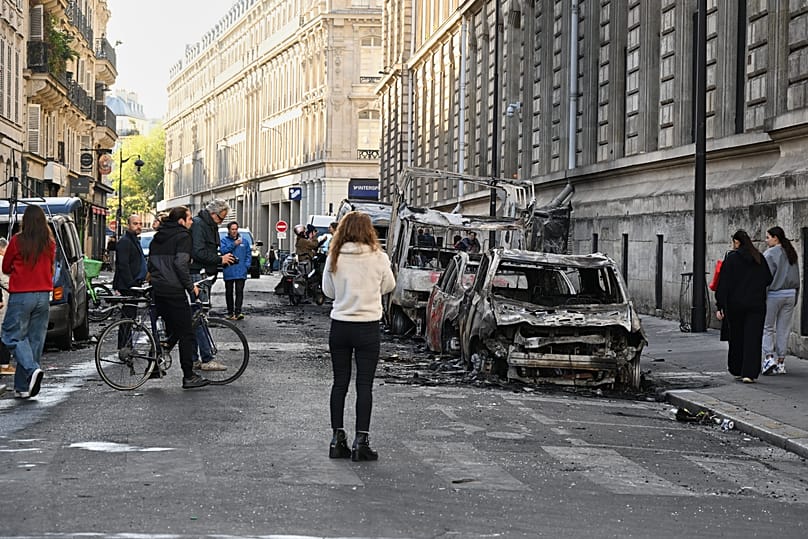 People look at charred cars the day after a demonstration against rising living costs, joining students' grievances, in Paris, Sunday, Oct. 18, 2026.